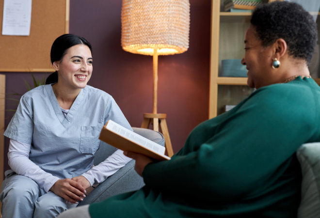 female caregiver smiling at an elderly woman holding a book