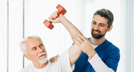 male physiotherapist helping an elderly man to lift a dumbbell