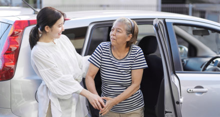 female caregiver assisting an elderly woman getting out of a car