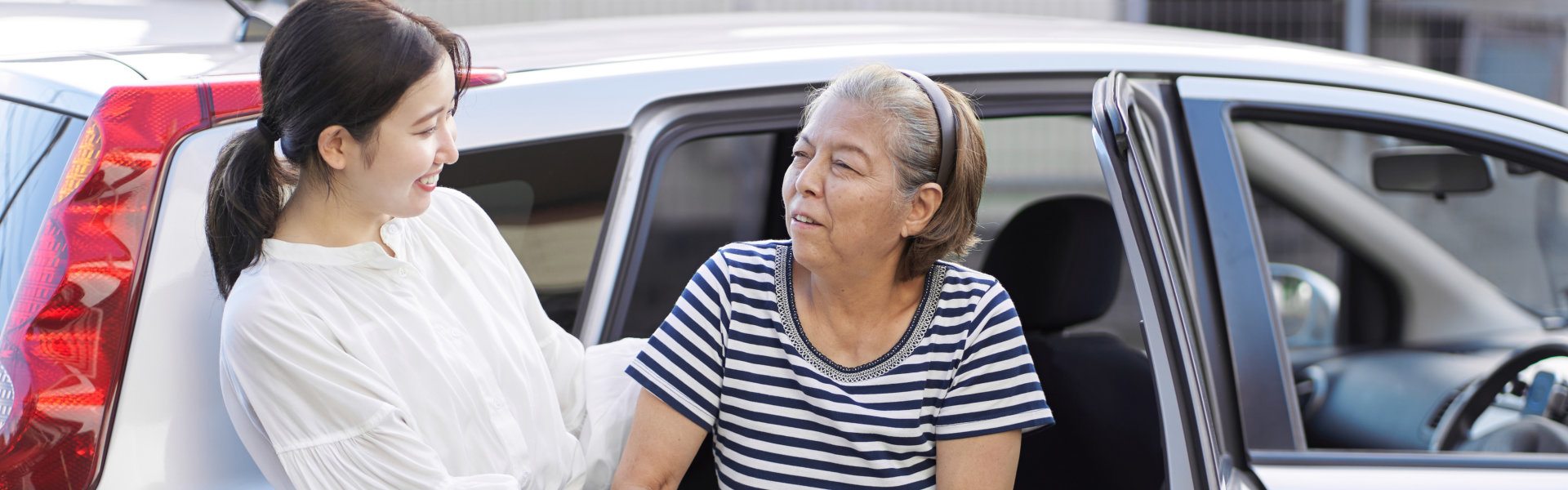 female caregiver assisting an elderly woman getting out of a car