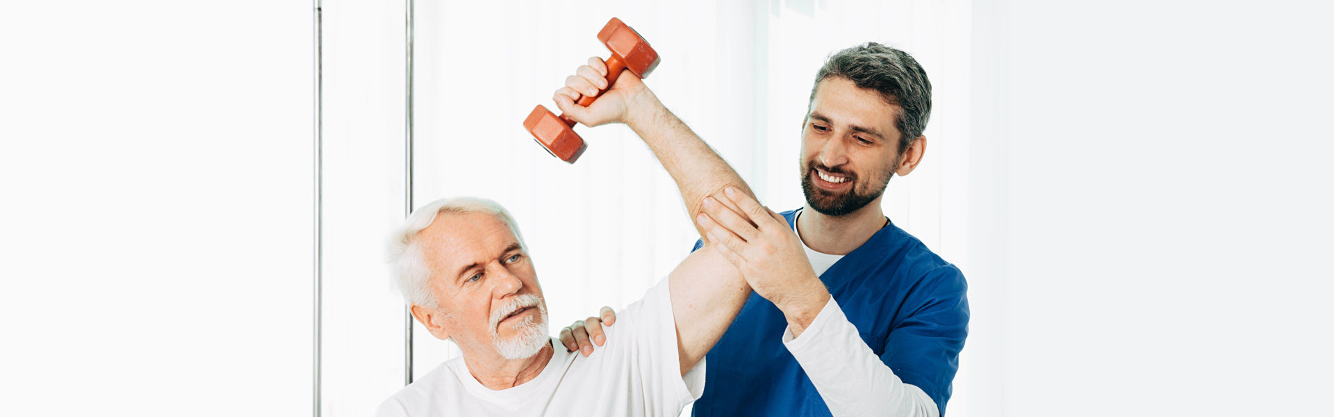 male physiotherapist smiling helping an elderly man to lift a dumbbell