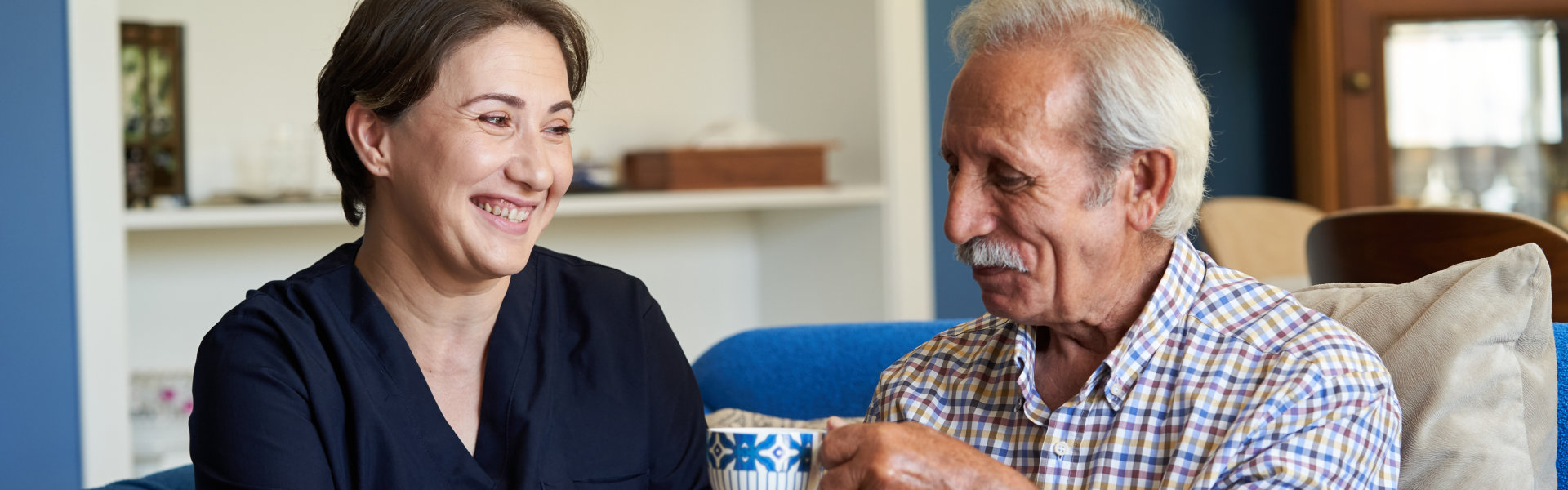 female caregiver smiling at an elderly man drinking tea