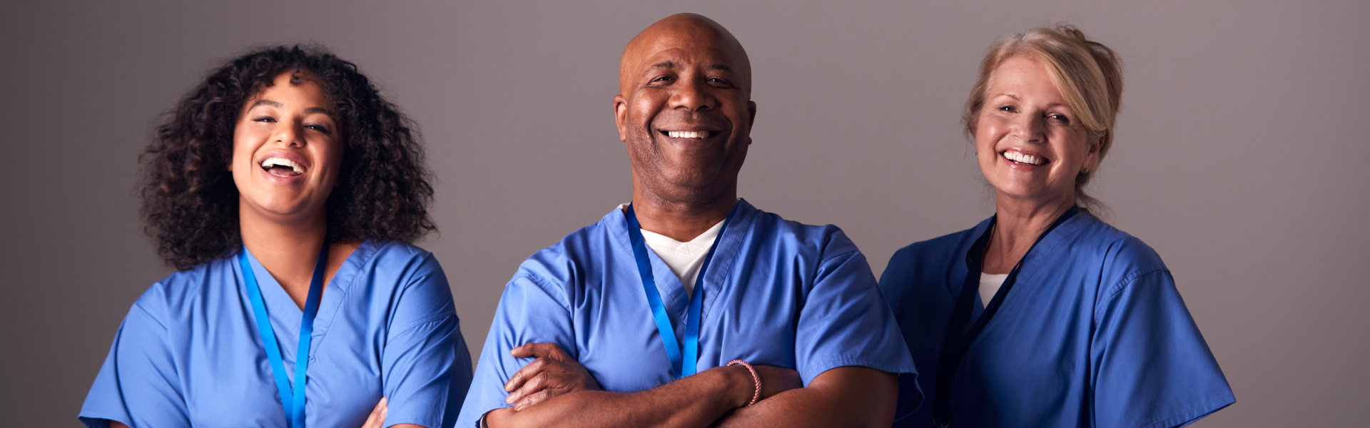 Studio Portrait Of Three Members Of Surgical Team Wearing Scrubs Standing Against Grey Background